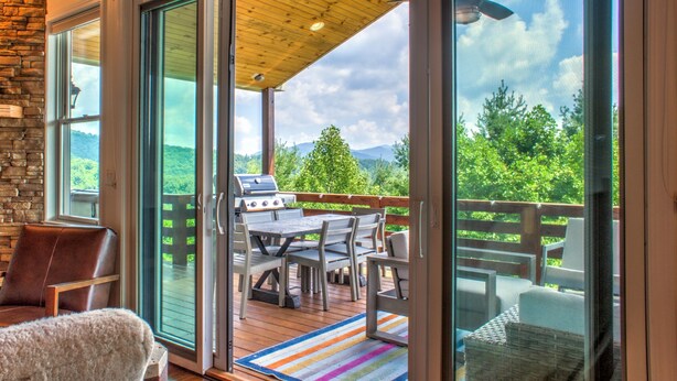 Um deck coberto ao ar livre, com churrasqueira, assentos e vista para a natureza.