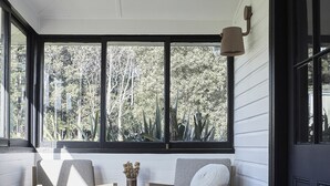 A cozy room with a large window, a round coffee table, and a sofa with cushions. - Benny’s Cottage  Luxury hinterland accomodation & photo shoot location (Clunes)