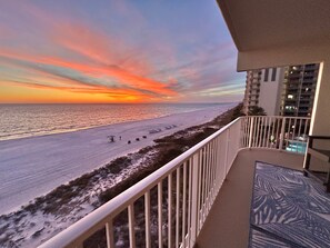 Un balcon avec vue sur une plage et l’océan au coucher du soleil.