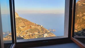 Une fenêtre donnant sur un paysage côtier, avec une colline parsemée de bâtiments et un ciel dégagé.