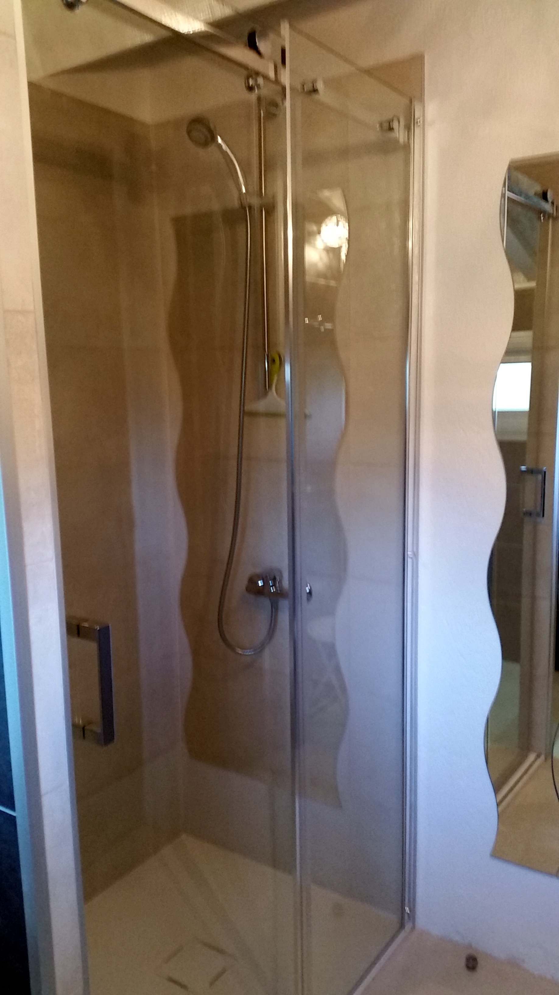 Eine moderne Duschkabine mit Glastür, Handbrause und wandmontiertem Wasserhahn.