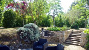 Eine Terrasse mit Korbmöbeln, Steinstufen und üppiger Bepflanzung.