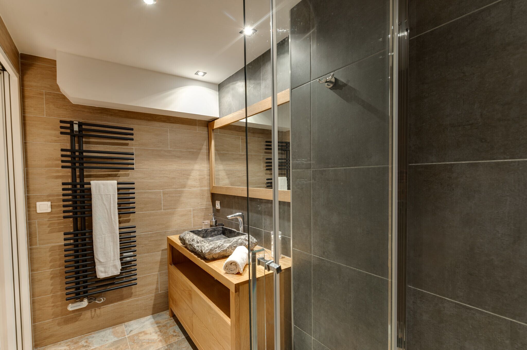 Une salle de bain moderne avec un meuble-lavabo en bois, une cabine de douche en verre et un porte-serviettes.