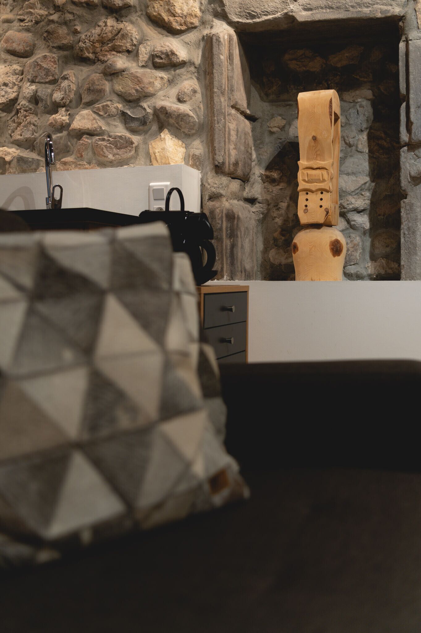 A bathroom with a stone wall, a wooden sculpture, and a patterned pillow.