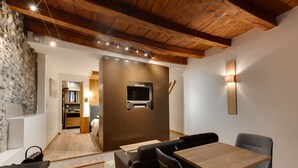 A modern interior with a wooden ceiling, a stone wall, a TV mounted on a wooden panel, and a dining area with a table and chairs. - La Cour Filaterie - A suite in the ❤️ of Annecy  🥐 breakfast included (Annecy)