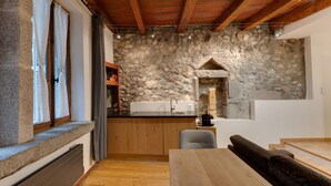 A rustic kitchen with stone walls, wooden beams, a stone fireplace, and a wooden dining table. - La Cour Filaterie - A suite in the ❤️ of Annecy  🥐 breakfast included (Annecy)
