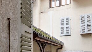 A narrow alleyway with a building featuring a balcony with potted plants and a wooden railing. - La Cour Filaterie - A suite in the ❤️ of Annecy  🥐 breakfast included (Annecy)