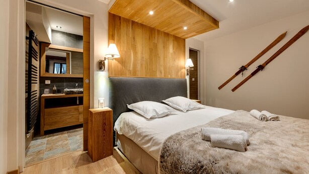 A modern bedroom with a large bed, wooden headboard, and a wooden ceiling. There are two bedside lamps, a wooden nightstand, and a bathroom visible through an open door. - La Cour Filaterie - A suite in the ❤️ of Annecy  🥐 breakfast included (Annecy)