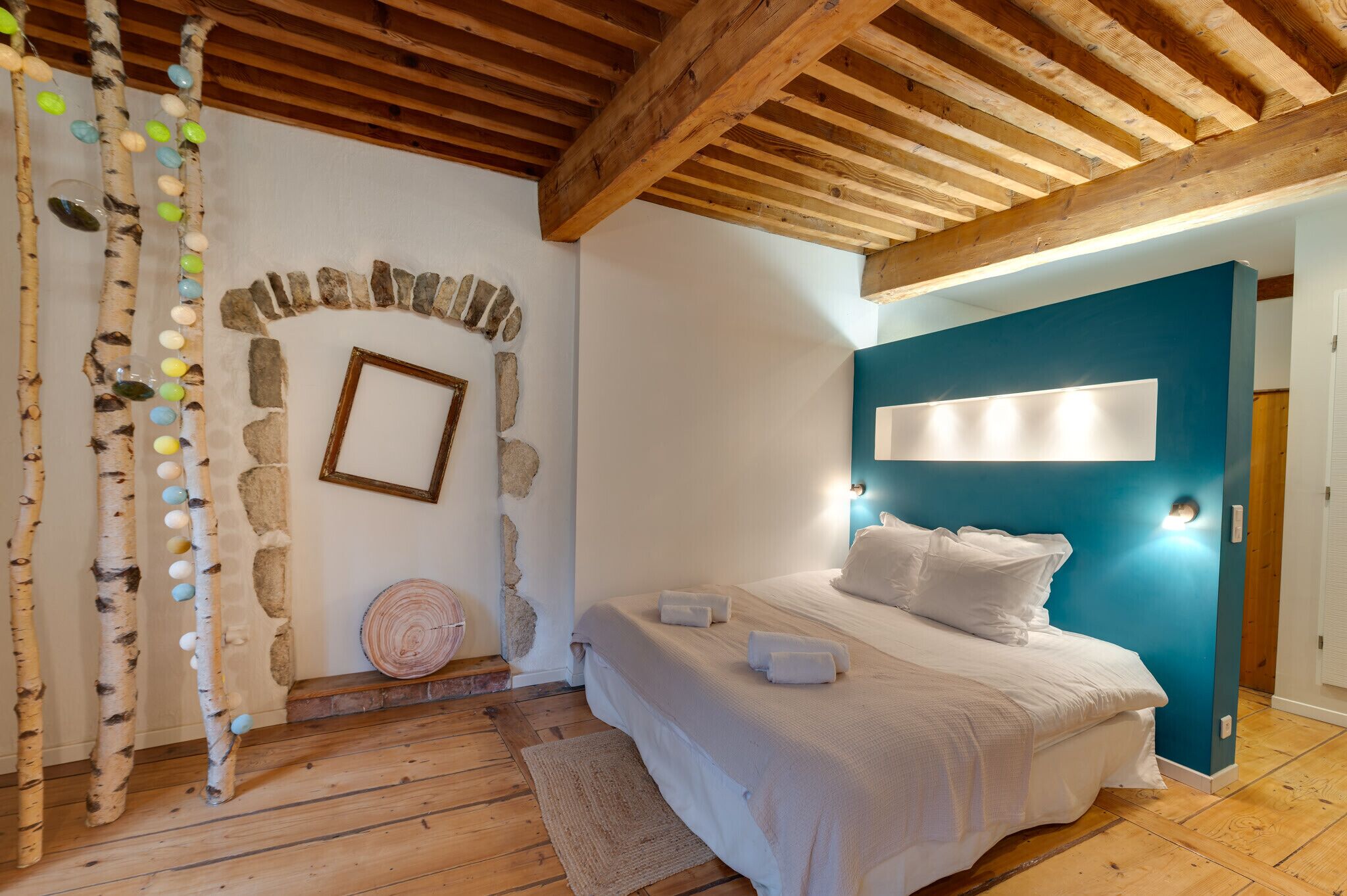 A bedroom with a wooden ceiling, a stone wall, a bed with white bedding, and a blue accent wall.