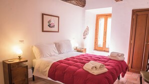 Een slaapkamer met een bed, nachtkastje, lamp, een ingelijste foto aan de muur en een raam met uitzicht.