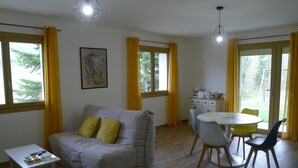 A cozy living room with a grey sofa, yellow cushions, a small white table, and a dining area with a round table and chairs.