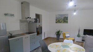 A compact kitchen with a microwave, oven, and sink. There is a dining area with a table and chairs, and a TV in the background.