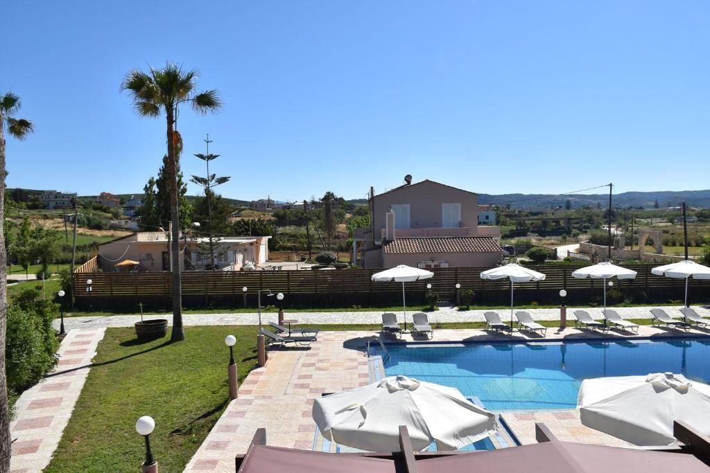 A swimming pool with lounge chairs and umbrellas, surrounded by a wooden fence, with buildings in the background.