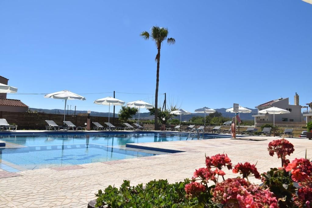 A swimming pool with lounge chairs and umbrellas, surrounded by potted plants and a clear sky.