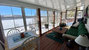 Un solárium con ventanas amplias, una mesa de madera, un sofá verde y vistas a un paisaje nevado.