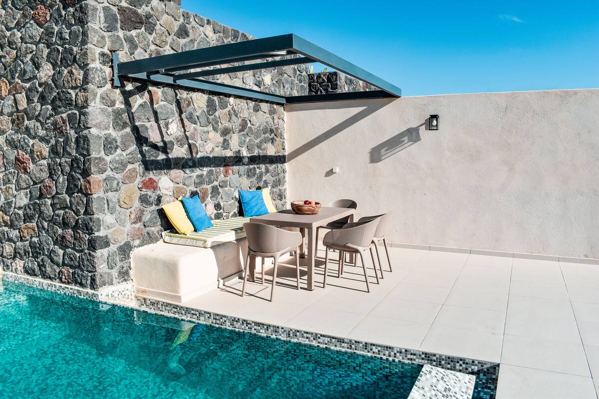 A poolside area with a stone wall, a pergola, and a table with chairs.