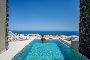 Une piscine offrant une vue dégagée sur l’océan, entourée de murs en pierre et de chaises longues blanches.
