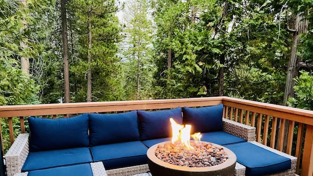 A deck with a fire pit, blue cushioned seating, and a wooden railing.