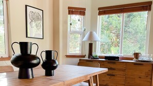 A wooden dining table with benches, a chandelier, and a view of the outdoors through large windows.