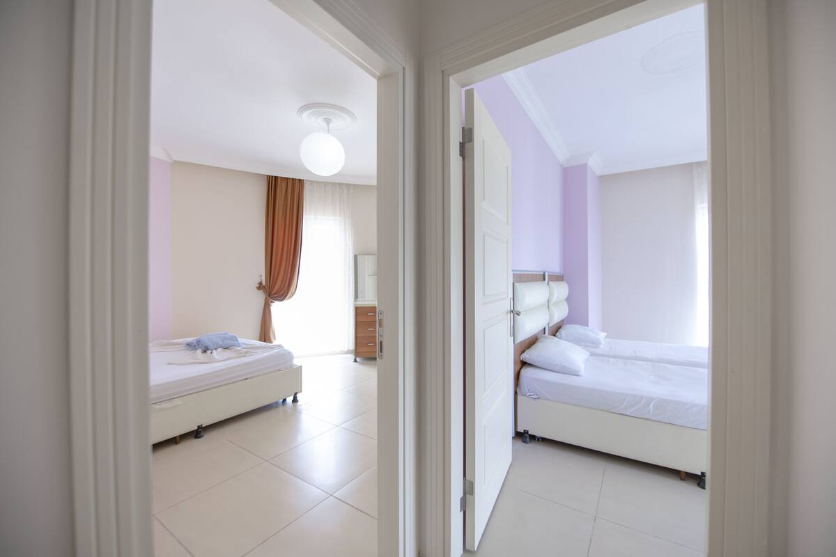 Ein Hotelzimmer mit zwei Betten, einer Deckenleuchte und Blick durch eine offene Tür.