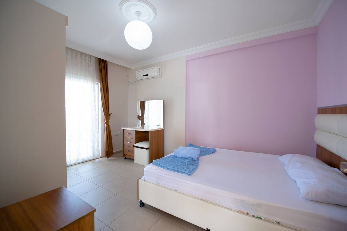 Ein Schlafzimmer mit Bett, Schreibtisch, Stuhl und einem Fenster mit Vorhängen.