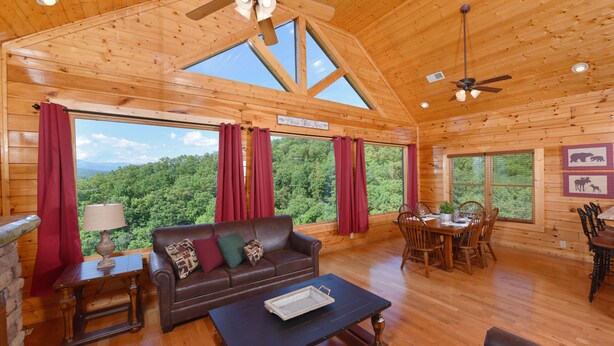 A spacious cabin with a large dining area, a cozy living room with a sofa and a coffee table, and large windows offering a view of the forest. - Legacy Mtn Resort Cabin w/ Mtn View - 2 King Beds + 2 Sofa Beds HotTub & Jacuzzi (Sevierville)