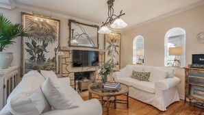 Una sala de estar con chimenea, sofás blancos, una mesa de centro y espejos decorativos.
