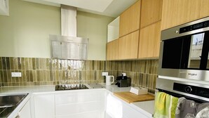Ett modernt kök med vita skåp, en rostfri köksfläkt, en inbyggd ugn och en mikrovågsugn.