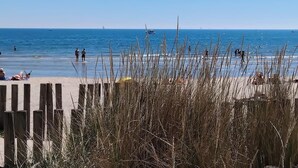 En strand med ett trästaket i förgrunden och människor i vattnet.