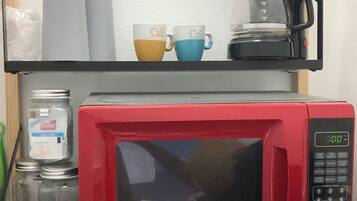 A red microwave on a shelf with two coffee cups and a coffee pot.