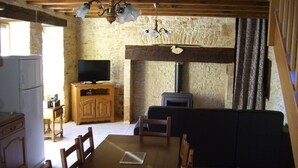 Un interior rústico con una mesa de comedor de madera, sillas, un televisor sobre un mueble de madera, un muro de piedra y una chimenea.