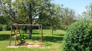 Un parque infantil con columpios y un pequeño jardín con un arbusto y una mesa cubierta.