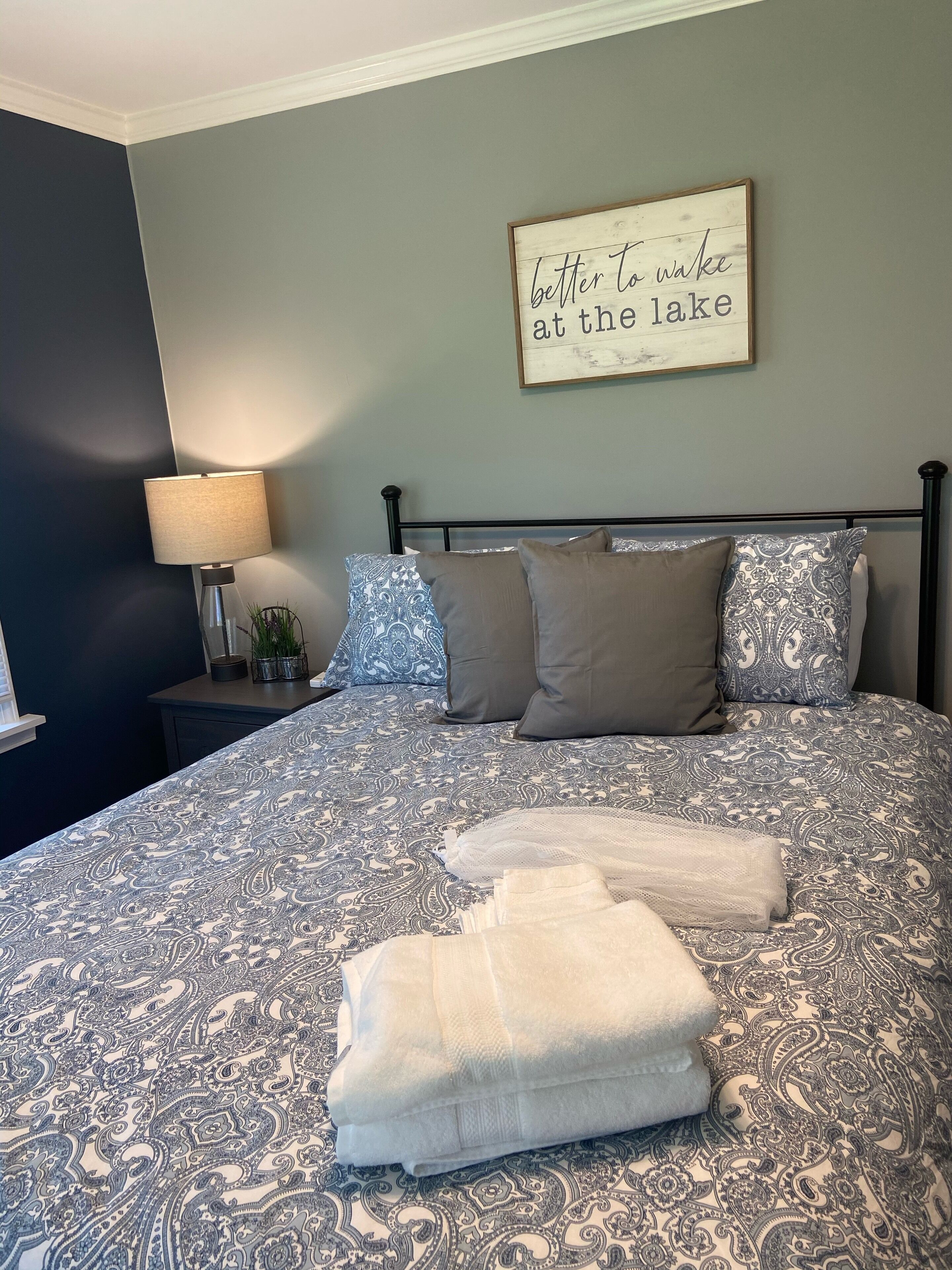A neatly made bed with a patterned bedspread, a bedside lamp, and a wall-mounted sign.