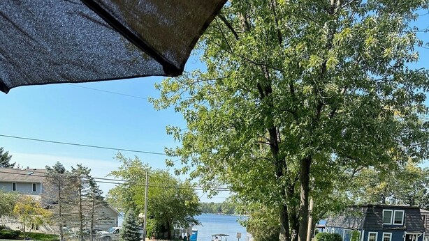 A deck with a grill, a flag, and a view of a lake and houses.
