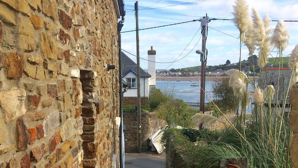 Un escalier étroit en pierre mène à un bâtiment dont un des murs est en pierre, et qui offre une vue sur la mer et les bateaux au loin.