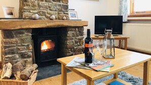 Un salon chaleureux avec une cheminée en pierre, un téléviseur et une table sur laquelle se trouvent une bouteille et des verres.
