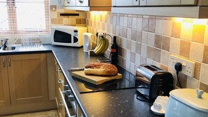 Une cuisine avec des meubles de rangement en bois, un four à micro-ondes, un grille-pain, une machine à pain et un pain sur le comptoir.