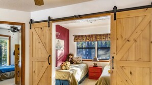 A bedroom with a bed, a nightstand, a window with a view, and a sliding barn door. - Spacious Angel Fire Cabin Near Skiing, Hiking, and Fishing (Angel Fire)