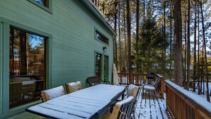 A wooden deck with a table and chairs, surrounded by a forest. - Spacious Angel Fire Cabin Near Skiing, Hiking, and Fishing (Angel Fire)