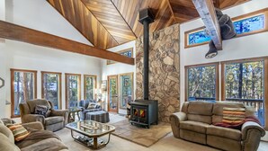 A spacious living room with a stone fireplace, large windows, and a high wooden ceiling. - Spacious Angel Fire Cabin Near Skiing, Hiking, and Fishing (Angel Fire)