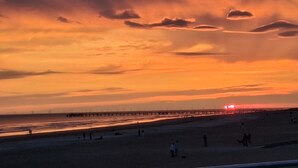 A beach with a pier extending into the water, people walking along the shore, and a sunset in the background. - CONTEMPORARY VILLA HEATED POOL CLOSE TO BEACH AND FOREST (Saint-Jean-de-Monts)