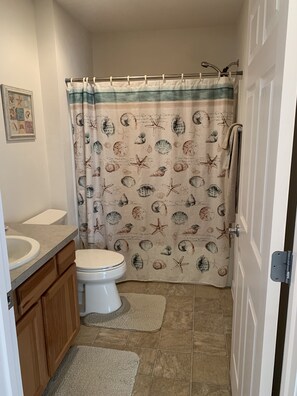 Un baño con inodoro, lavabo y cortina de ducha con estampado de conchas marinas y estrellas de mar.