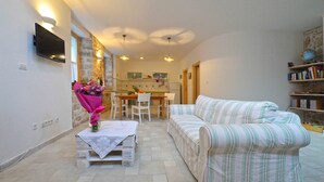 A cozy living room with a sofa, a dining table, and a TV mounted on the wall. - Frantoio House. Charming stone house in front of the dock (Betina)
