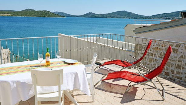 A terrace with a table set for two, a bottle of wine, and two red lounge chairs. - Frantoio House. Charming stone house in front of the dock (Betina)
