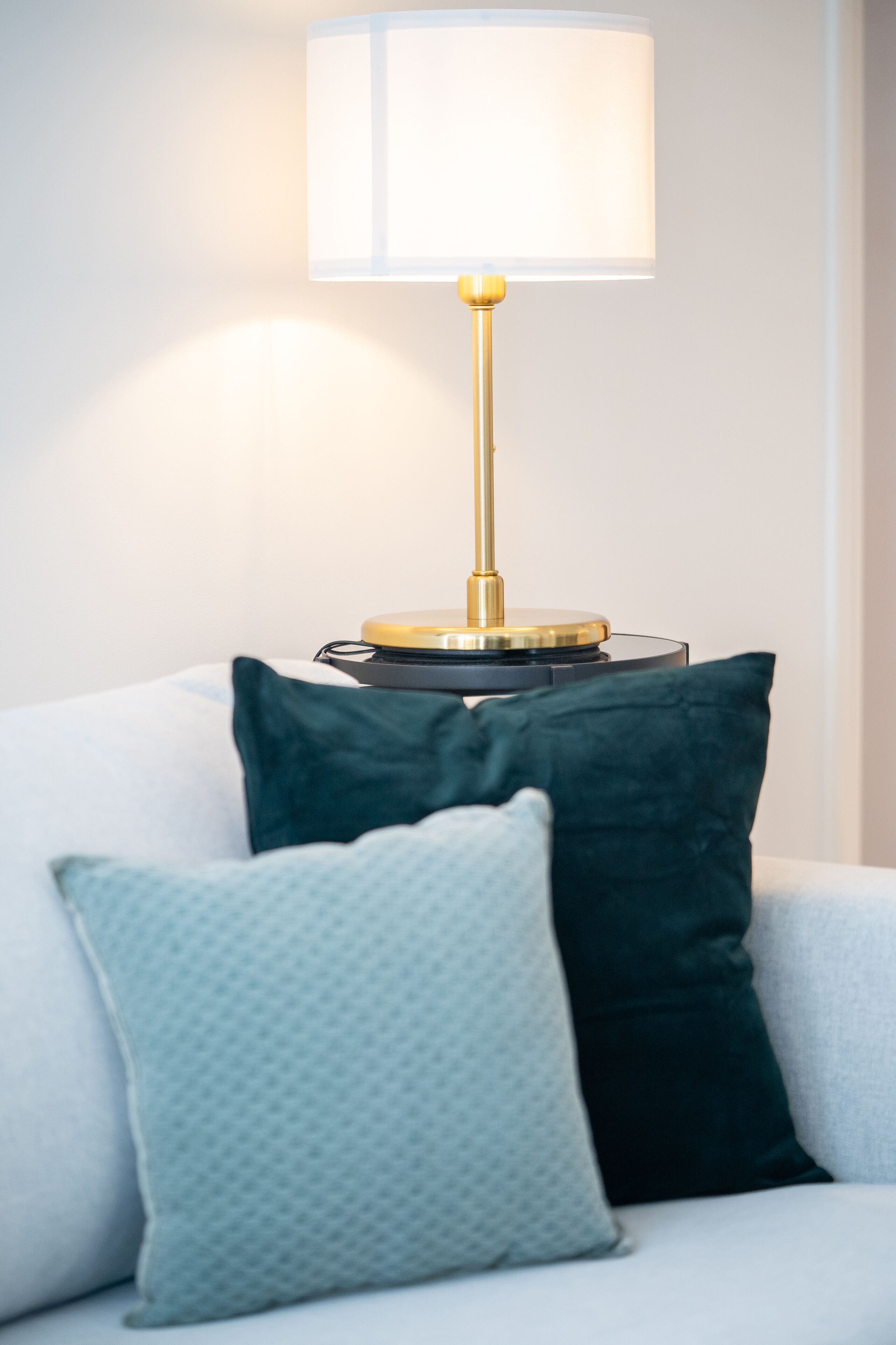 A modern lamp with a white shade and a gold base on a round table.
