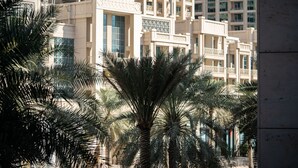 A modern building with multiple balconies and large windows, surrounded by palm trees. - HiGuests - Boulevard Crescent Tower 2 (Dubai)