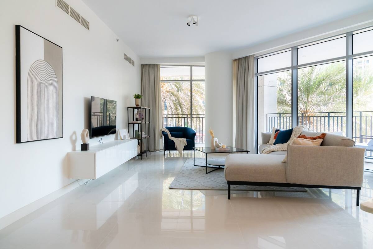 A modern living room with a large window, a sofa, a TV, and a bookshelf.