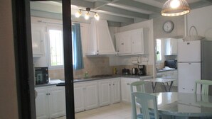 A kitchen with white cabinets, a dining table, chairs, a refrigerator, and a hanging light fixture. - Le Pijolin (Saint-Justin)