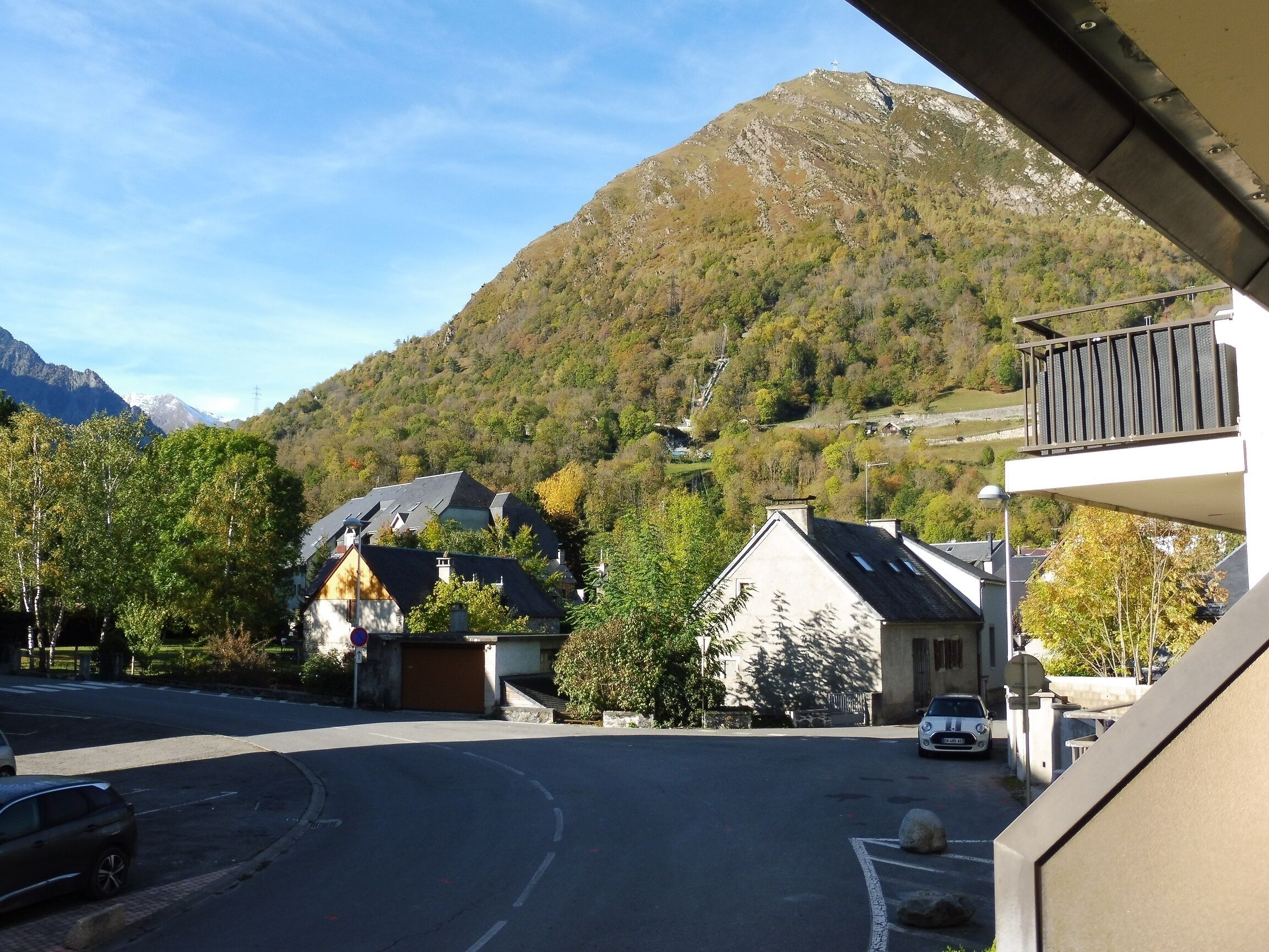 Un espace de stationnement avec une montagne en arrière-plan, un bâtiment doté d’un balcon et une voiture garée devant.