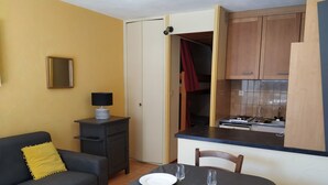 Un espace de vie compact comprenant un coin repas, une kitchenette et un canapé agrémenté d’un coussin jaune.